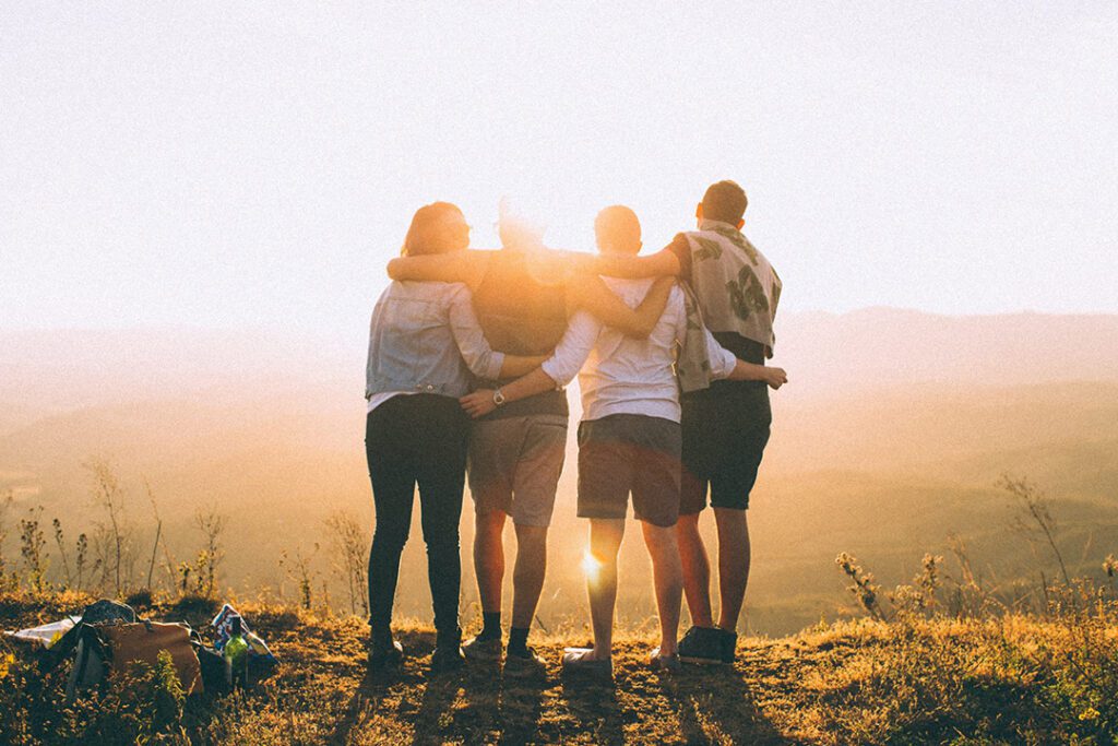 An image of friends with their arms around each other as they face the sunset.