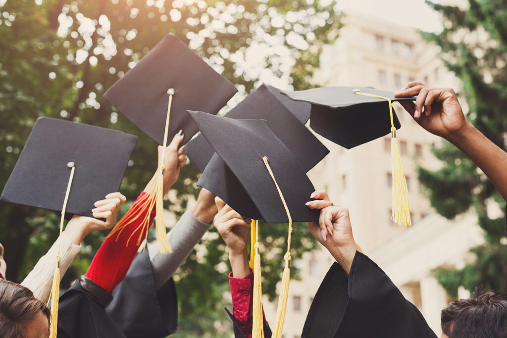 An image of multiple hands throwing their graduation caps up in the air in celebration.