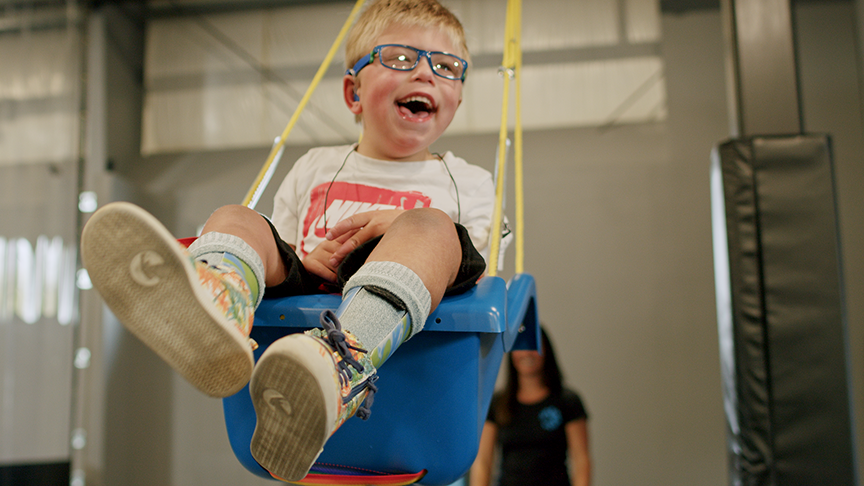 An image of a young child with special needs swinging happily on a swing.