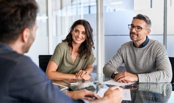 Smiling mature couple meeting with bank manager for investment. Beautiful mid adult woman with husband listening to businessman during meeting in conference room in modern office. Happy middle aged couple meeting loan advisor to buy a new home.