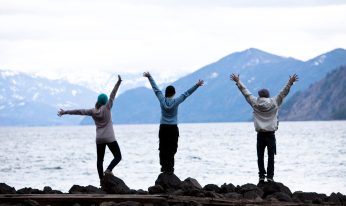 A group of three young adults standing with their arms open at the edge of Lake Pend Oreille in Sandpoint, Idaho.