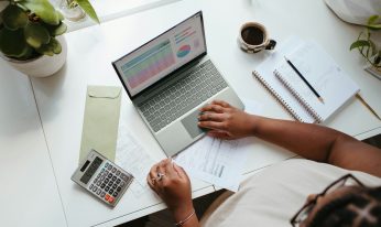 Hands type on a laptop near a calculator and budgeting papers.